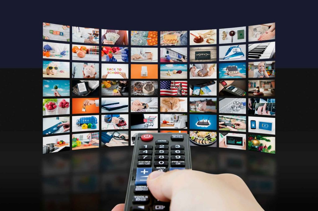 Hand mit Fernbedienung vor einer Wand aus Fernsehbildern